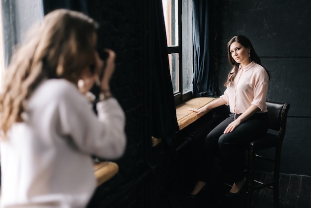 Modelo de mulher posando sentado na cadeira no estúdio fotográfico para uma fotógrafa irreconhecível