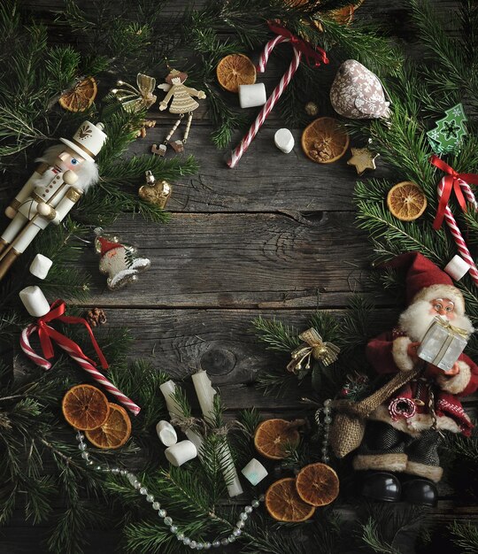 Modelo de Natal com brinquedos, galhos de pinheiro, laranjas, doces em fundo escuro de tábuas de madeira.