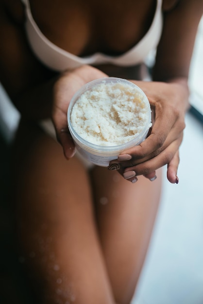 Modelo de pele negra vestido de cueca segura uma jarra com um esfoliante