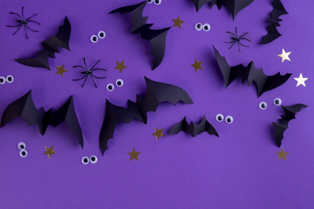 Modelo de quadro de Halloween com morcegos de papel preto e olhos assustadores de plástico em um fundo colorido roxo.