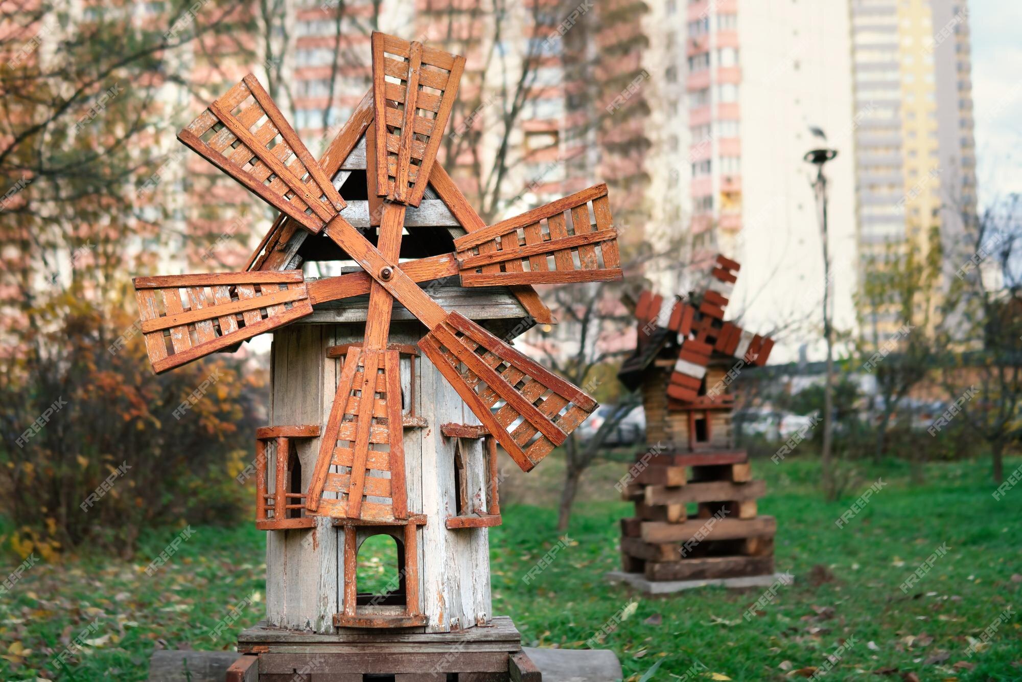 Maquete de um moinho de vento medieval de madeira em um parquinho infantil  com uma casa ao fundo