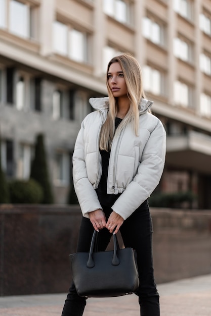 modelo de uma jovem com uma jaqueta branca e uma bolsa de couro da moda fica na cidade