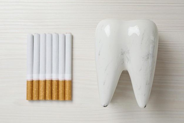 Modelo de diente dañado y cigarrillos en la mesa de madera blanca plana