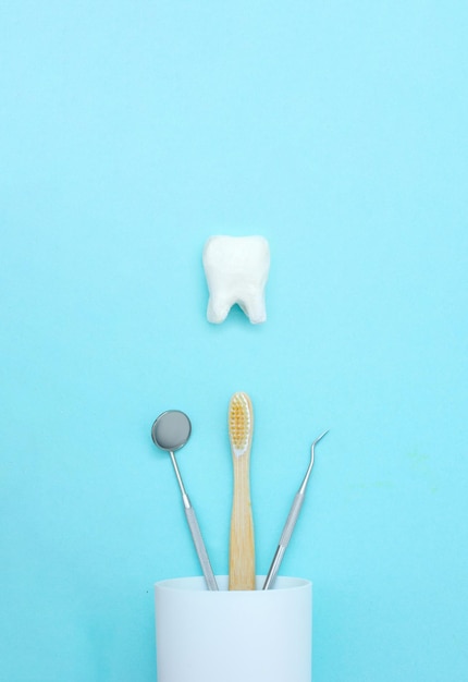 Modelo de diente dental con equipo de odontología médica de metal herramientas dientes dentista boca espejo cepillo de dientes en vidrio blanco