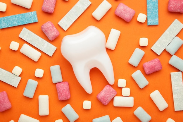 Modelo de diente sano blanco y montón de gomas de mascar sobre fondo naranja Concepto de higiene dental oral