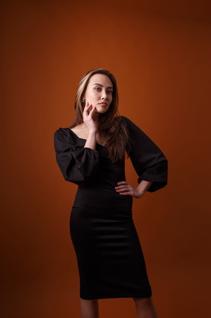 Modelo elegante com vestido preto com decote profundo posando em fundo laranja