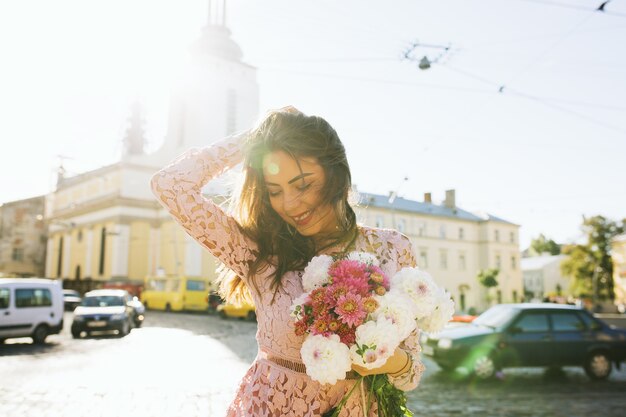 Modelo elegante e sorridente com vestido de renda segurando um buquê de flores