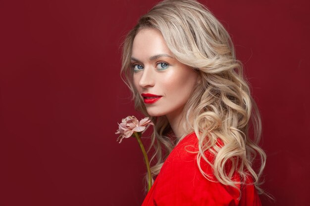 Modelo elegante mulher com maquiagem e cabelo encaracolado saudável em fundo vermelho retrato de beleza