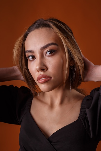 Foto modelo elegante con vestido negro con escote profundo posando sobre fondo naranja