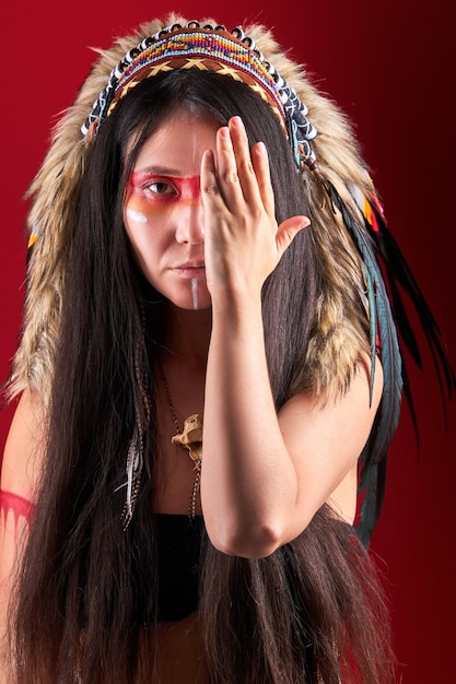 Modelo em indiano vestindo e posando de maquiagem colorida, com penas na cabeça. roupa dos povos indígenas das américas, mulher étnica fechando o rosto