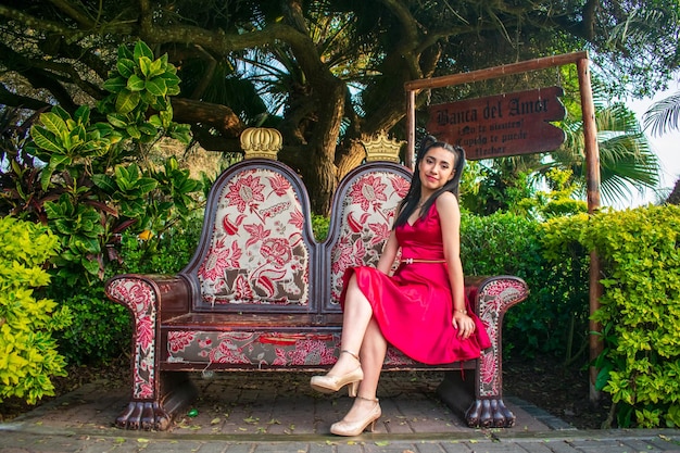 Foto modelo em um vestido vermelho sentado em uma poltrona em um parque.