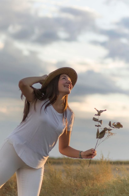 Foto modelo encantador segurando flores brancas e posando alegremente no fundo de um campo rural