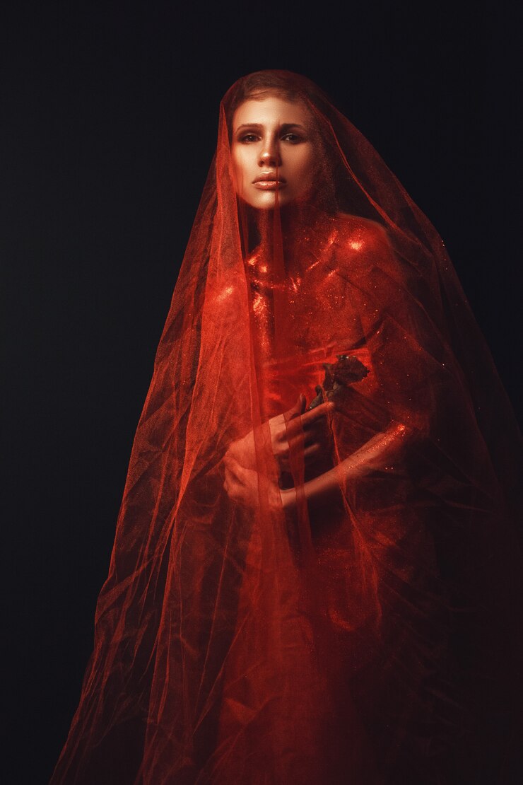 Foto modelo está posando em um quarto escuro com um longo tecido vermelho
