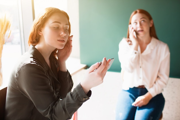 La modelo femenina se toma una selfie en un café y su amiga habla por teléfono. Las mujeres jóvenes están sentadas en un café.