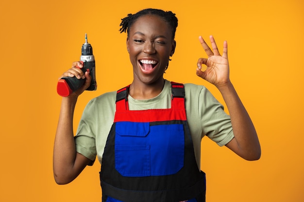 Modelo femenino afroamericano negro en uniforme sosteniendo una herramienta de reparación de destornilladores contra la espalda amarilla