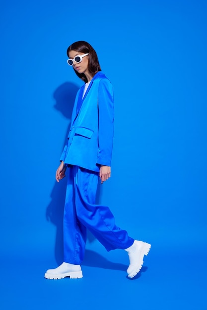 Modelo femenino asiático de moda con traje azul botas blancas y gafas de sol