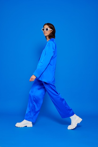 Modelo femenino asiático de moda con traje azul botas blancas y gafas de sol