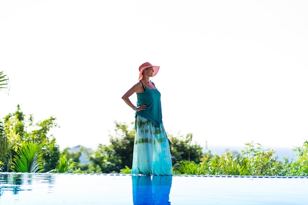 modelo femenino con sombrero y vestido de pie en una piscina