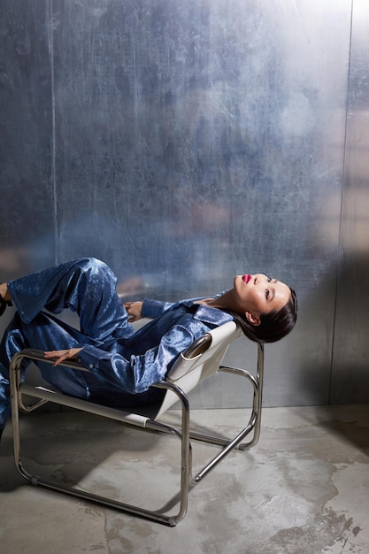 Modelo feminino asiático de moda em terno azul brilhante posando em localização futurista moderna metálica