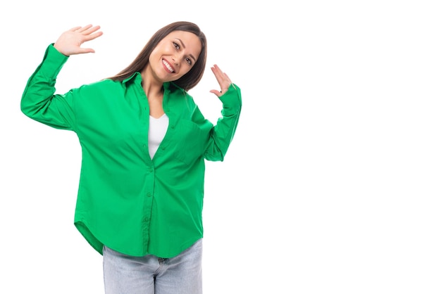 Modelo feminino de cabelos castanhos brilhante e alegre com olhos castanhos em uma camisa verde posando em um branco