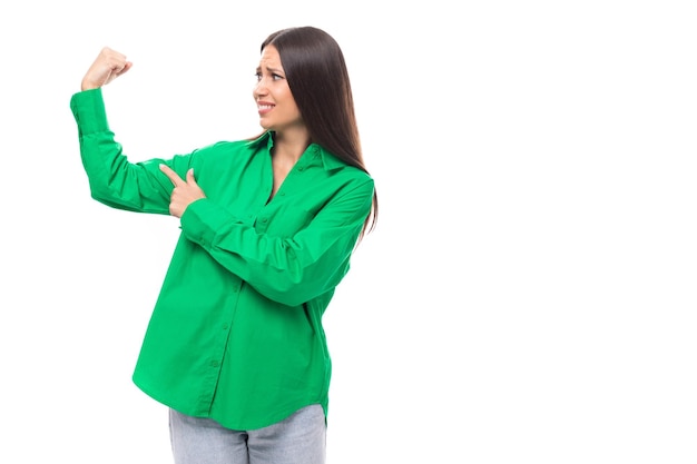 Modelo feminino esbelto de cabelos castanhos com olhos castanhos em uma camisa verde mostra bíceps