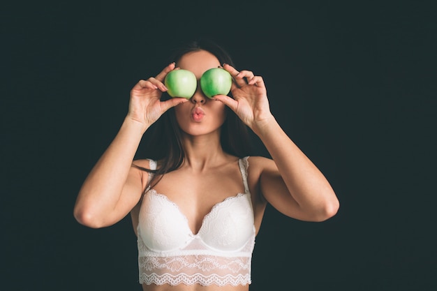 Modelo feminino fechar com maçã verde fresca. Garota vegetariana de dieta. A jovem mulher tem o cabelo preto longo isolado. A menina tem uma figura esportiva, ela vestia roupas íntimas brancas.