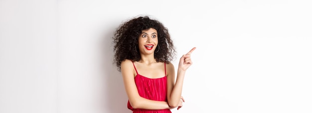 Modelo feminino surpreso com cabelos cacheados e maquiagem apontando o dedo e olhando para a esquerda com um sorriso divertido