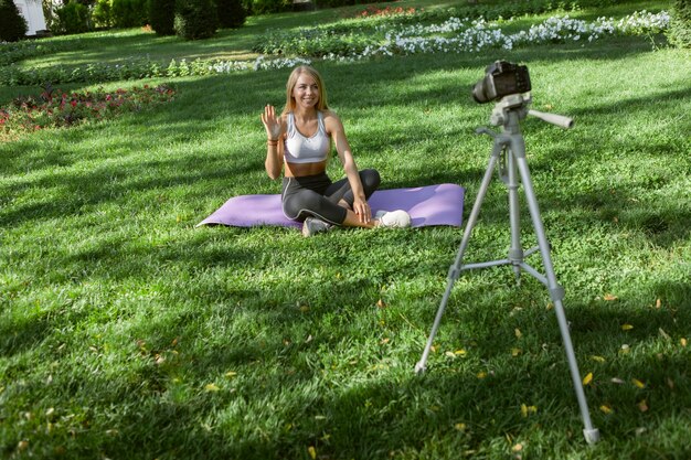 Modelo de fitness alegre joven blogueando en cámara en el parque al aire libre