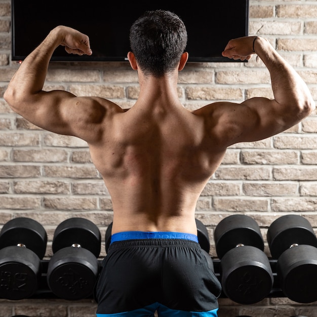 Modelo de fitness hombre atlético fuerte posando músculos de la espalda, tríceps en el gimnasio