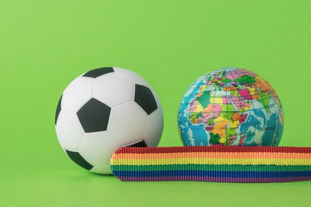 Foto un modelo del globo terráqueo, un balón de fútbol y una cinta lgbt sobre un fondo verde. el concepto de lgbt en el fútbol. espacio para texto.