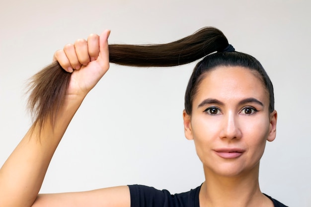 Modelo hermosa chica con cabello largo recto marrón brillante. Productos para el cuidado del cabello. Mantiene el cabello en un puño, fuerza del cabello