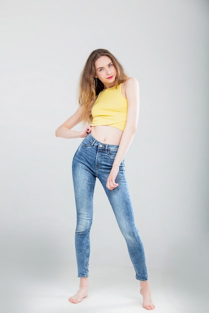 Modelo hermosa joven en jeans ajustados y top en estudio sobre fondo blanco