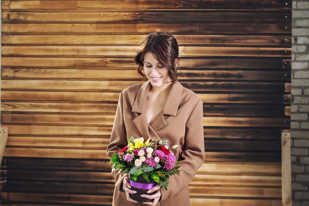 Modelo hermosa joven con ramo de flores sobre fondo de madera