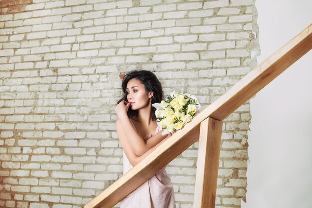 Modelo hermosa joven con ramo de flores sobre fondo de pared de ladrillo