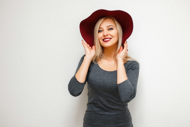 Modelo hermosa mujer feliz con sombrero en vestido gris junto a la pared blanca