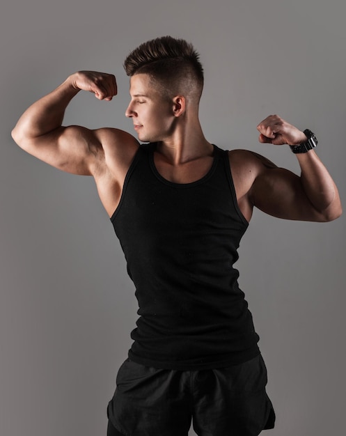 Modelo de hombre guapo musculoso fuerte con peinado en camiseta negra con cuerpo musculoso atlético sobre fondo oscuro en el estudio Dieta y cuerpo deportivo saludable