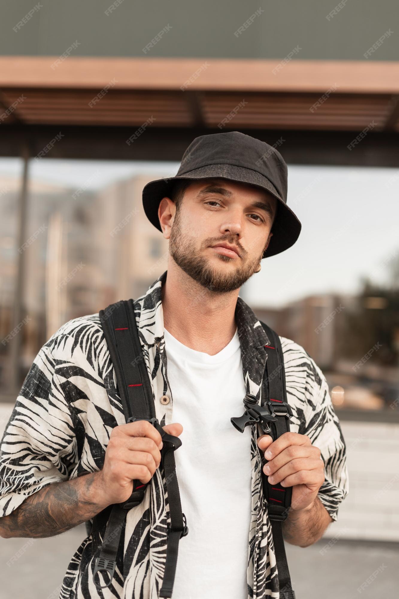 Modelo de hombre hipster con sombrero de moda en ropa elegante y mochila viaja en ciudad guy camina por la calle | Foto Premium