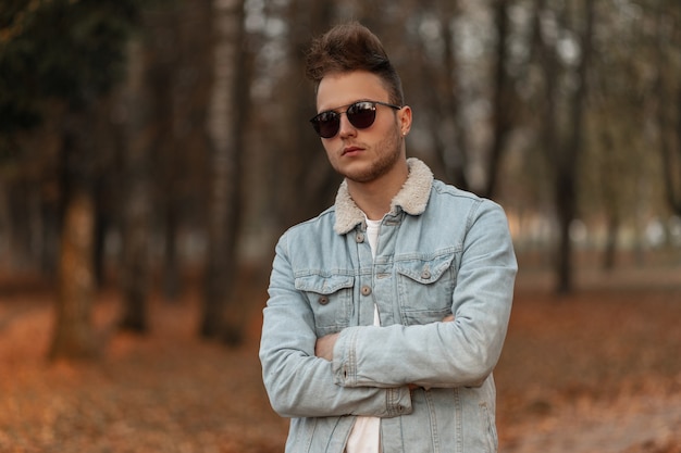 Modelo de hombre joven en una elegante chaqueta azul de mezclilla posando en el parque