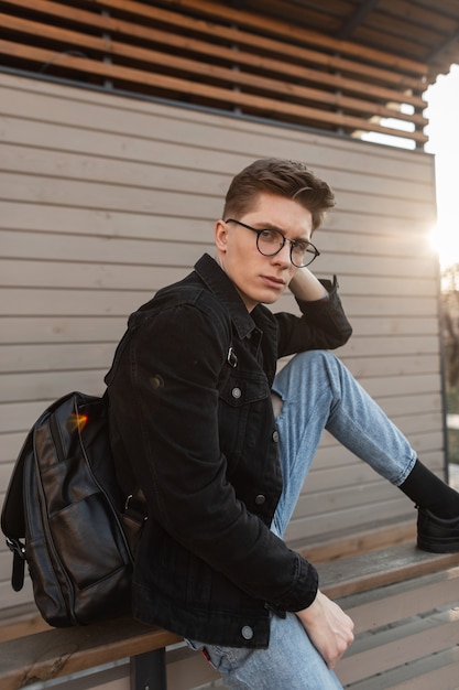 Modelo de hombre joven de moda con peinado en ropa casual de mezclilla con estilo en gafas con estilo