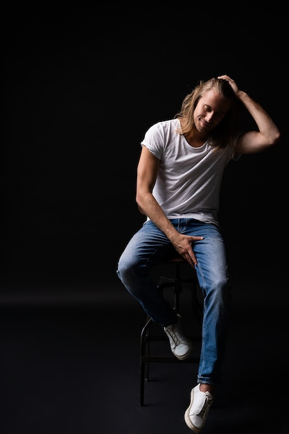 Modelo de hombre de moda elegante sentado en la silla aislada en negro