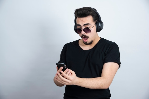 Modelo de hombre morena en gafas de sol y auriculares con teléfono móvil.