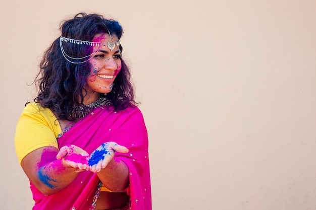 Modelo indiano feminino sorriso branco de neve no festival de cores holimulher indiana no tradicional vestido de sari com cabelo preto encaracolado em uma pintura rosa e azul e joias bindi celebrando o festival de cores holi