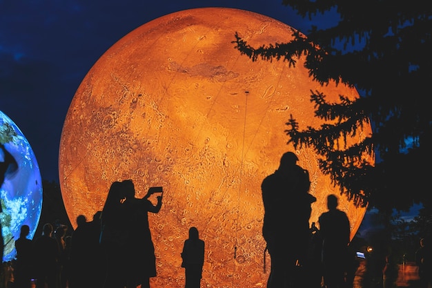 Foto modelo inflable gigante del planeta marte de noche con siluetas de personas. superficie del planeta rojo marte. colonización de marte.