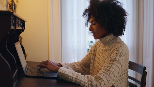 Modelo inspirado mandando mensagens para laptop no local de trabalho de madeira, senhora de cabelo encaracolado conversando