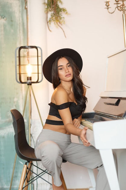 Foto modelo jovem quente sentado em frente ao piano e olhando para a câmera foto de alta qualidade