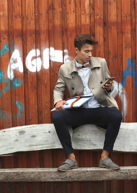 Modelo jovem usando telefone celular enquanto está sentado em um banco