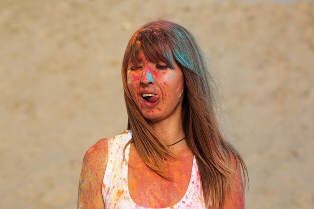 Modelo joven divertido cubierto con pintura seca naranja Holi en el desierto