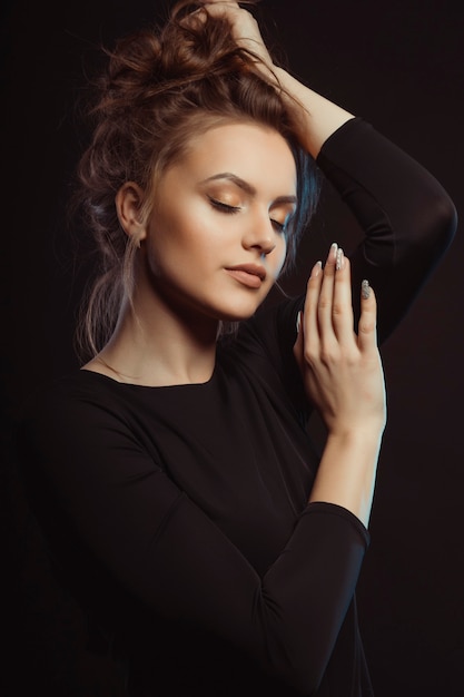 Modelo joven de lujo en vestido negro posando en el estudio con los ojos cerrados