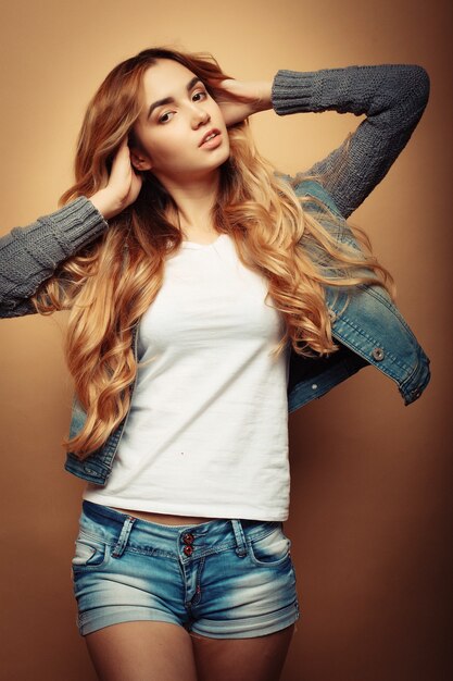 Modelo joven de moda en ropa bonita posando en el estudio en la pared amarilla