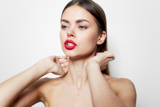 Foto modelo labios rojos hombros desnudos piel limpia de manos cerca de la cara maquillaje brillante fondo claro